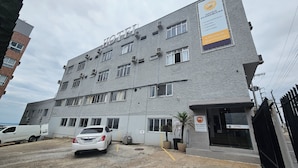A hotel building with multiple floors, air conditioning units, and a parking area with a white car. - Ok Inn Hotel Florianópolis (Florianópolis)