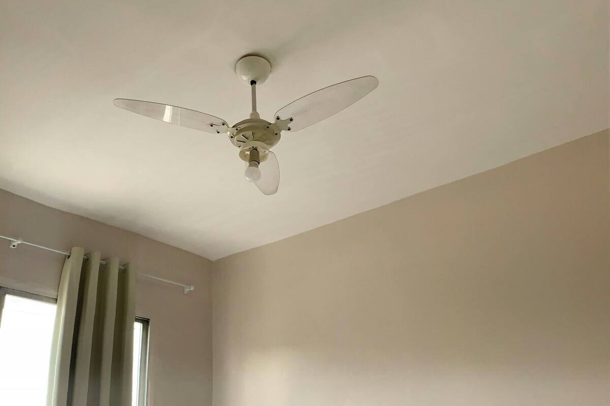 A hotel room with two beds, a ceiling fan, a window with curtains, and a view of the city.