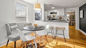 A modern kitchen with white cabinets, a central island, and a dining area with a gray sofa and white chairs.