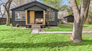 A small, dark-colored wooden house with a front porch, a wooden door, and a window.