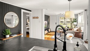 A modern kitchen with a central island, a hanging light fixture, and a view of the living area.