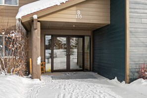 L’entrée d’un hôtel, avec un porche en bois, une porte-fenêtre coulissante et un toit recouvert de neige.