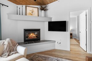 A modern living room with a fireplace, a mounted TV, and a cozy seating area.