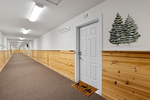 A hallway with wooden paneling, a white door marked with the number 13, and a welcome mat with a deer silhouette.