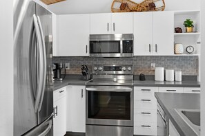 Una cocina moderna con electrodomésticos de acero inoxidable, armarios blancos y un salpicadero de ladrillo.
