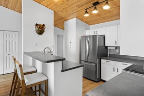 A modern kitchen with white cabinets, a stainless steel refrigerator, and a wooden ceiling.
