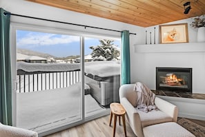 A cozy living room with a fireplace, a sofa, and a view of a snowy landscape through a sliding glass door.