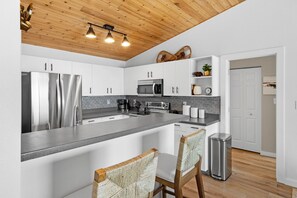 Une cuisine moderne avec des meubles blancs, des appareils en acier inoxydable, un plan de travail en granit et un plafond en bois.