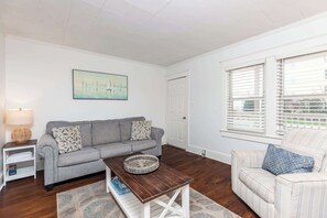 Una sala de estar con un sofá gris, un sillón a rayas, una mesa de centro de madera y un cuadro en la pared.