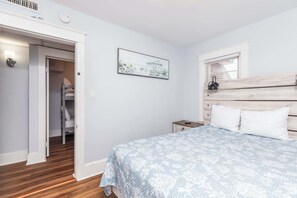 Un dormitorio con cama, mesita de noche, cabecera de madera, un cuadro y armario con espejo.