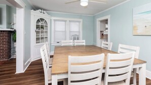 A dining room with a wooden table, white chairs, a ceiling fan, and a brick fireplace.