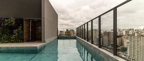A rooftop swimming pool with a city view, a glass railing, and a modern building facade.