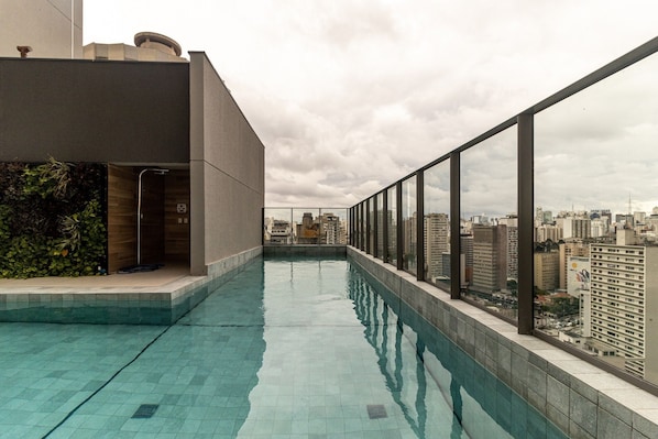 A rooftop swimming pool with a city view, a glass railing, and a modern building facade.