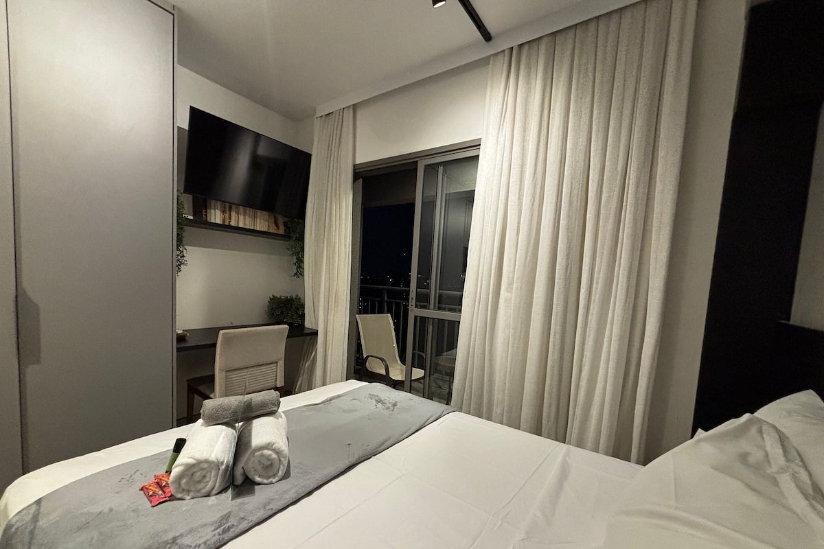 Een hotelkamer met een bed, bureau, stoel en raam met gordijnen.