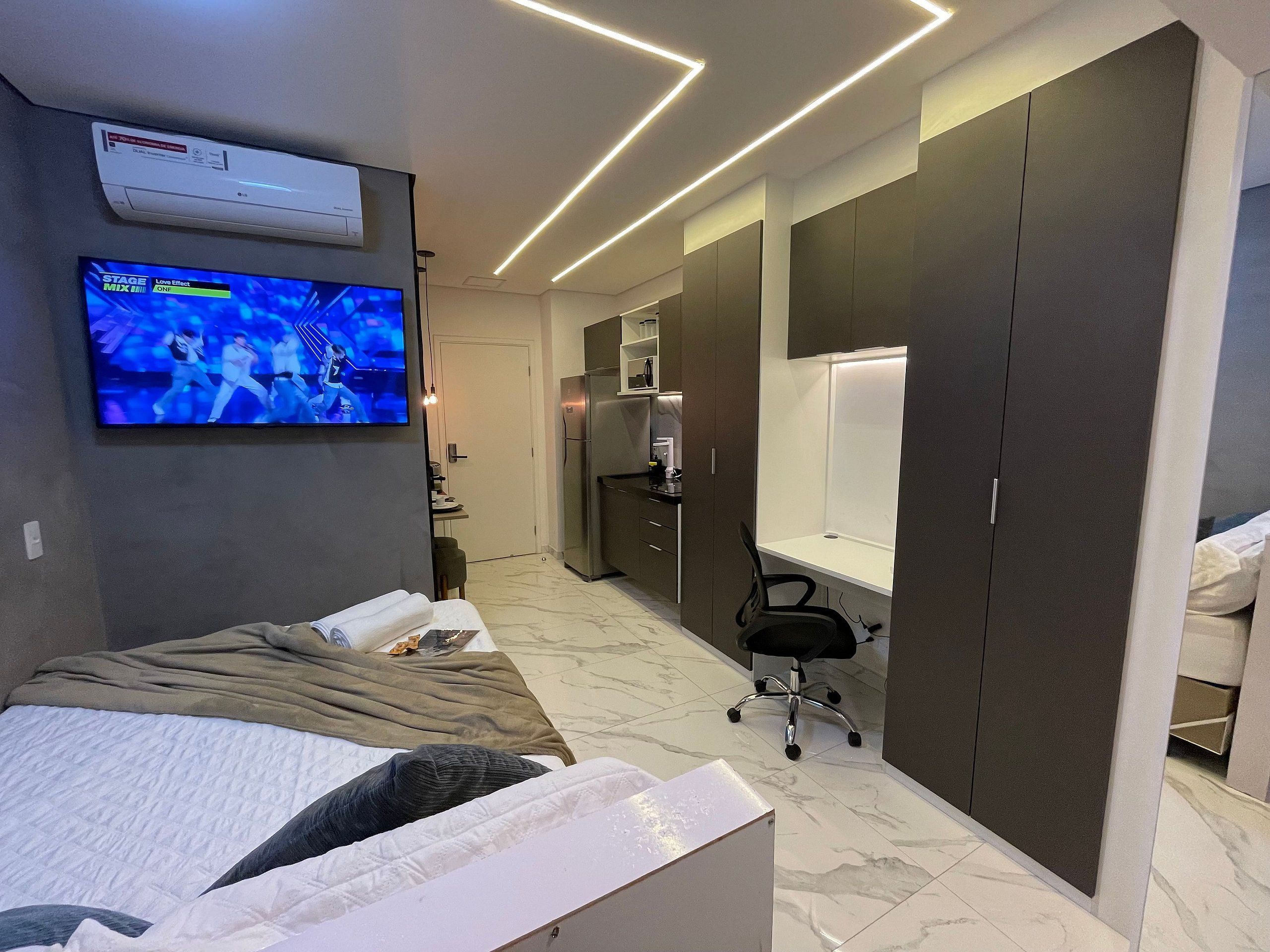 A modern bedroom with a TV, a bed, a desk, and a wardrobe.