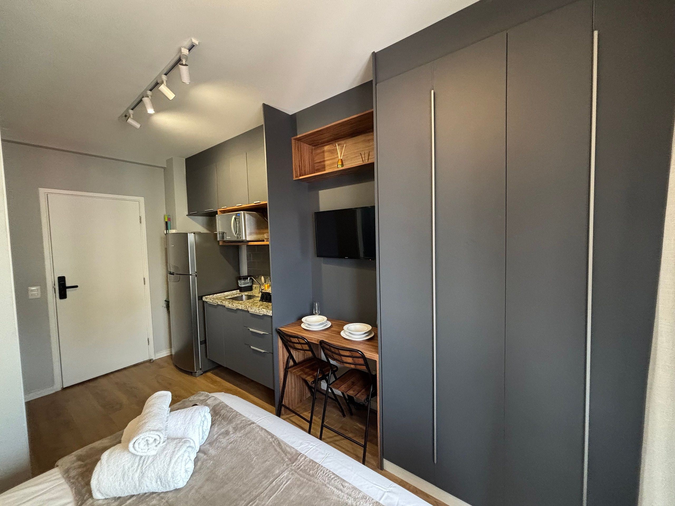 Quarto compacto com cama, escrivaninha pequena e cozinha compacta.