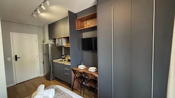Quarto compacto com cama, escrivaninha pequena e cozinha compacta.
