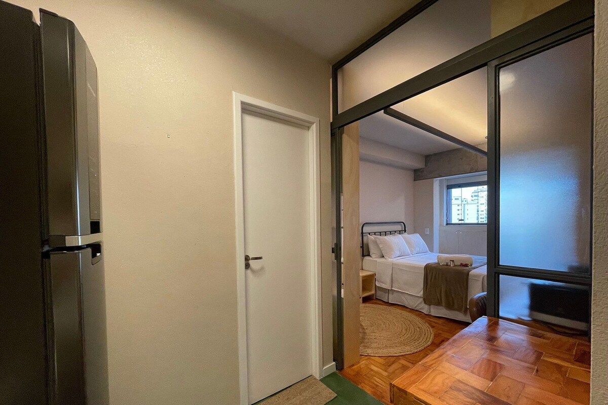 A bedroom with a bed, a window, a wooden floor, and a door.