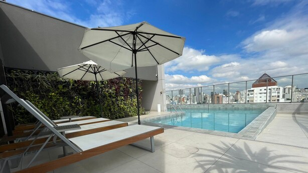 A rooftop pool with lounge chairs and umbrellas, a city view, and a modern building facade. - Prime Stay - Vila Buarque - São Paulo - BR (São Paulo)