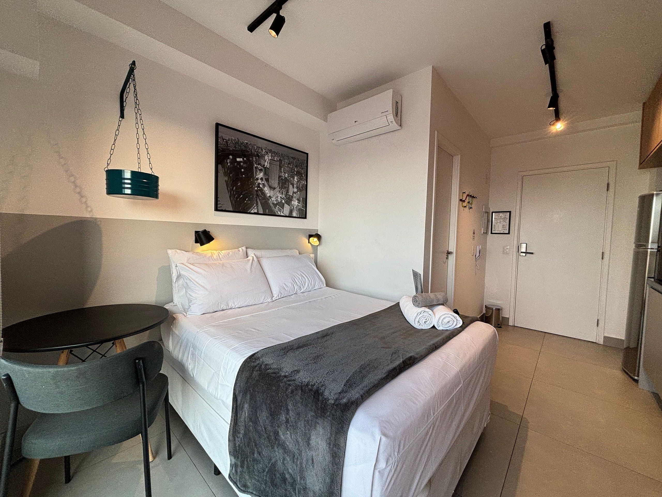 A hotel room with a bed, a desk, a chair, a picture on the wall, and a door.