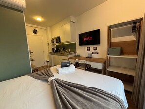 Une chambre d’hôtel équipée d’un lit, d’un bureau, d’une télévision, d’une kitchenette et d’une armoire.