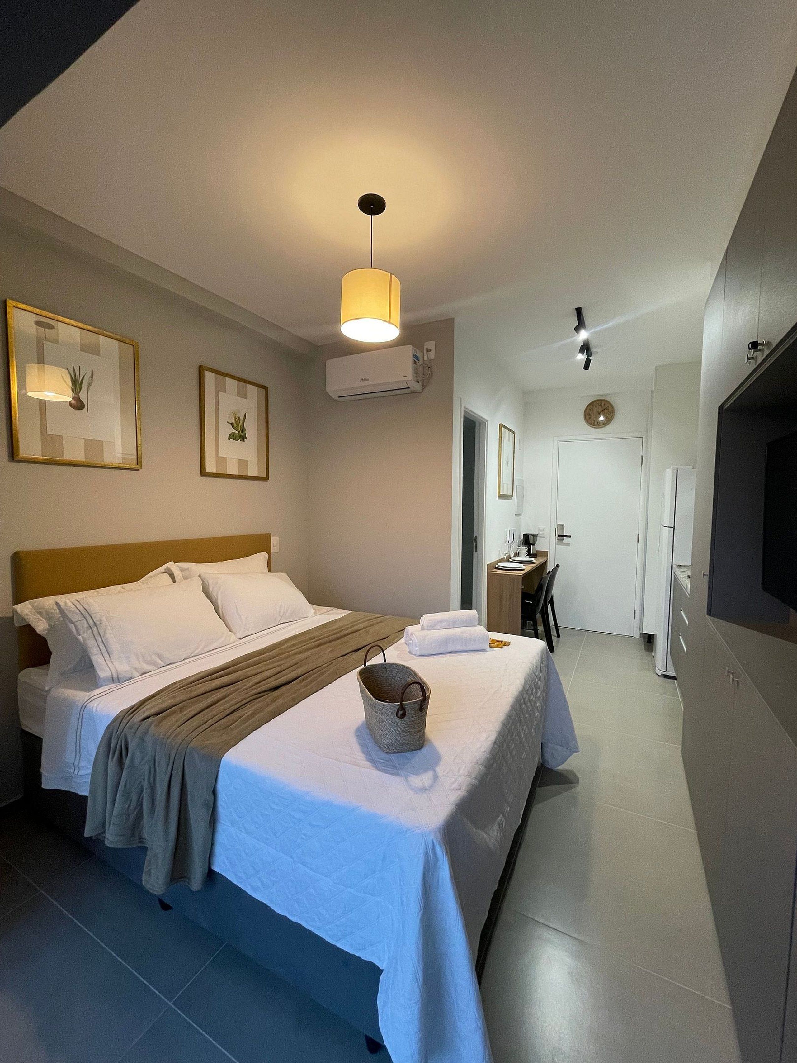 A hotel room with a bed, bedside table, lamp, air conditioning unit, and a view of the hallway.