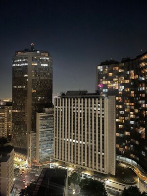 A nighttime cityscape with high-rise buildings, one featuring a grid of windows and another with a curved facade.