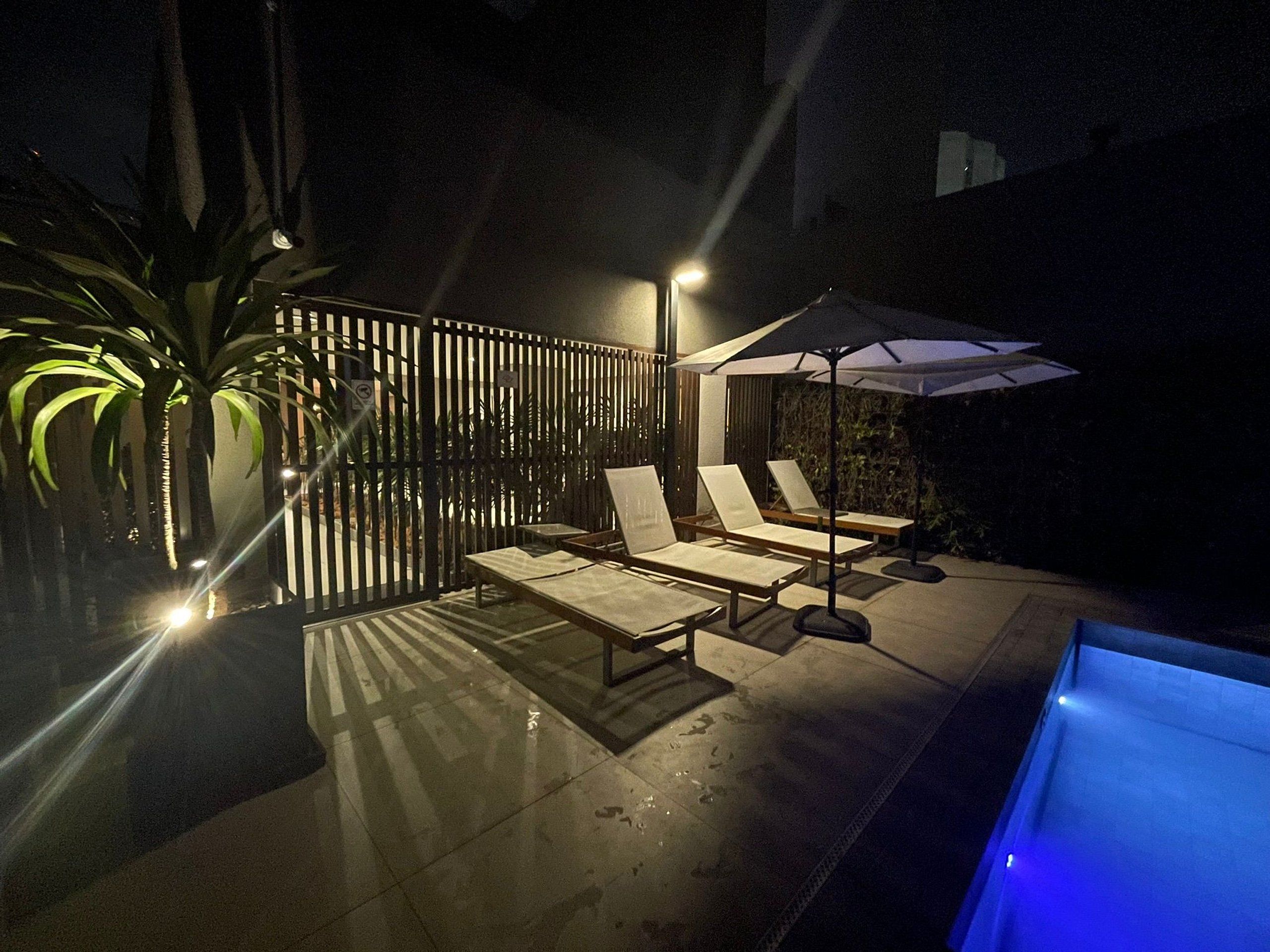 An outdoor pool area with lounge chairs, a table, and a fence.