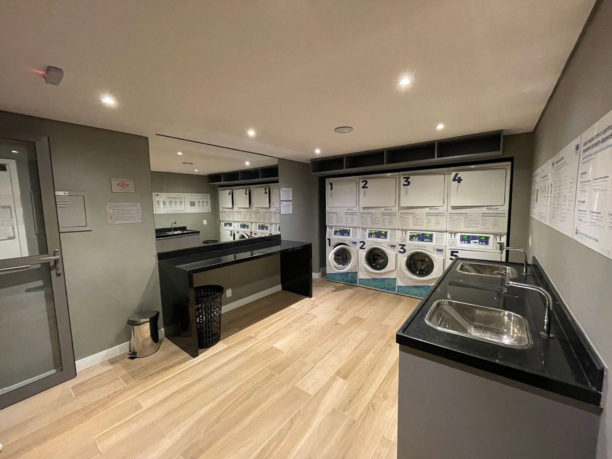A laundry facility with multiple washing machines, a sink, and a trash bin.