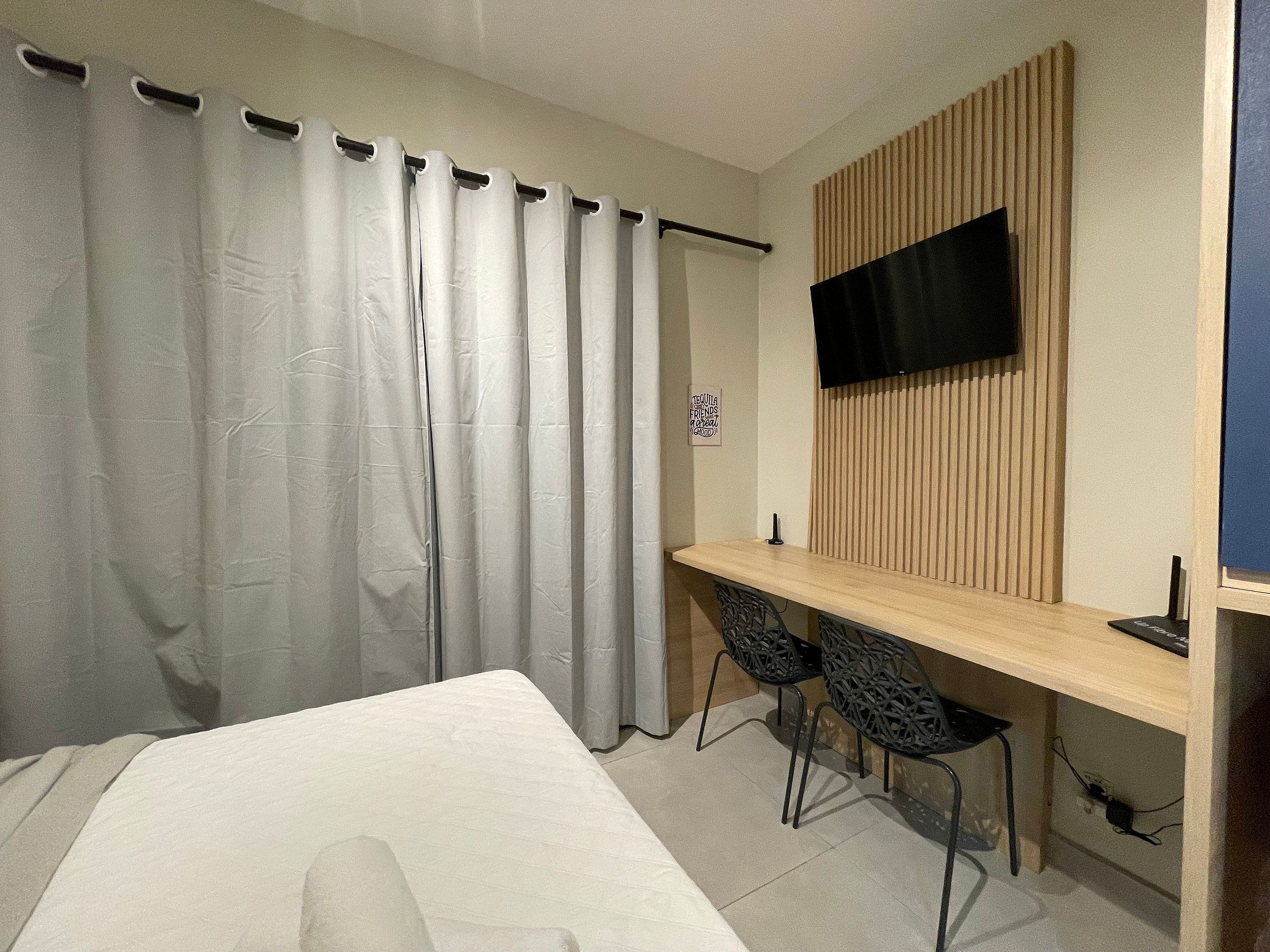 Ein Schlafzimmer mit einem Bett, einem Schreibtisch, zwei Stühlen, einem Fernseher und einem Vorhang.