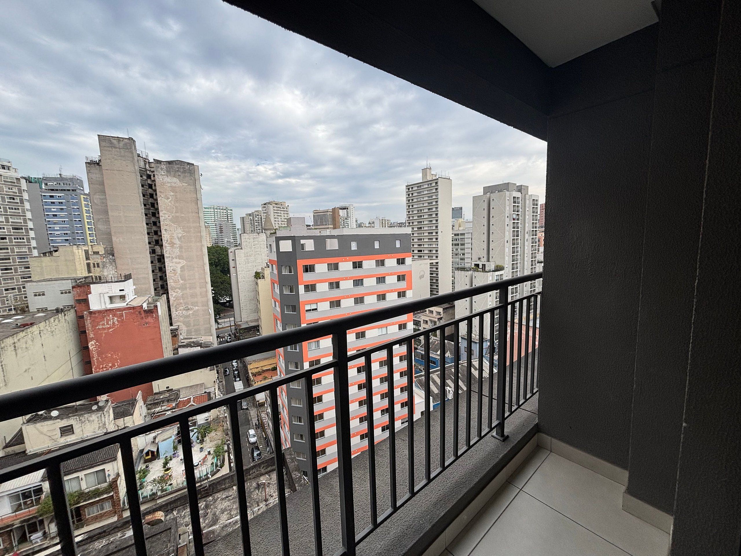 A balcony with a view of high-rise buildings, a tiled floor, and a metal railing.