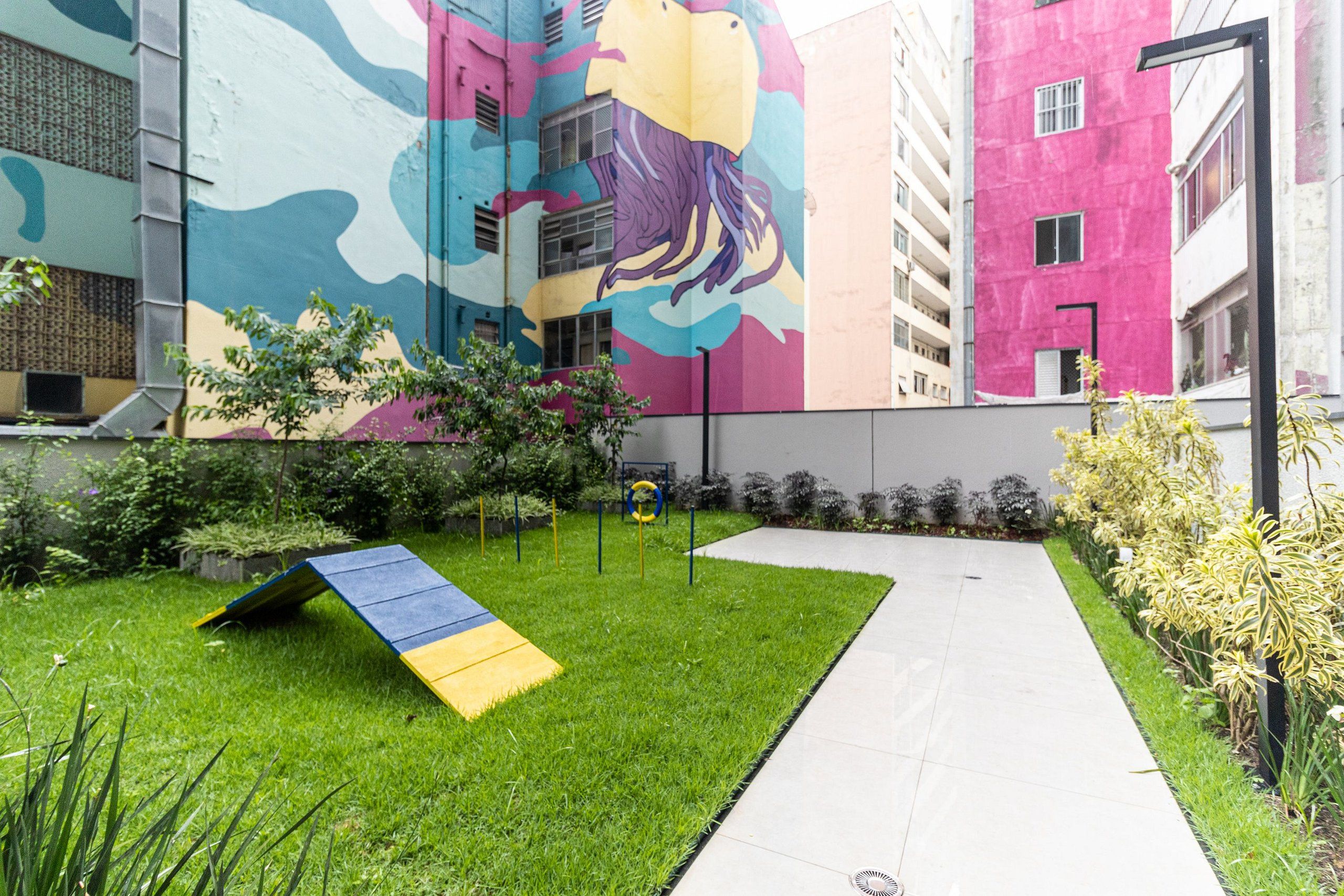 Un patio con césped, un sendero y un mural colorido en un edificio.