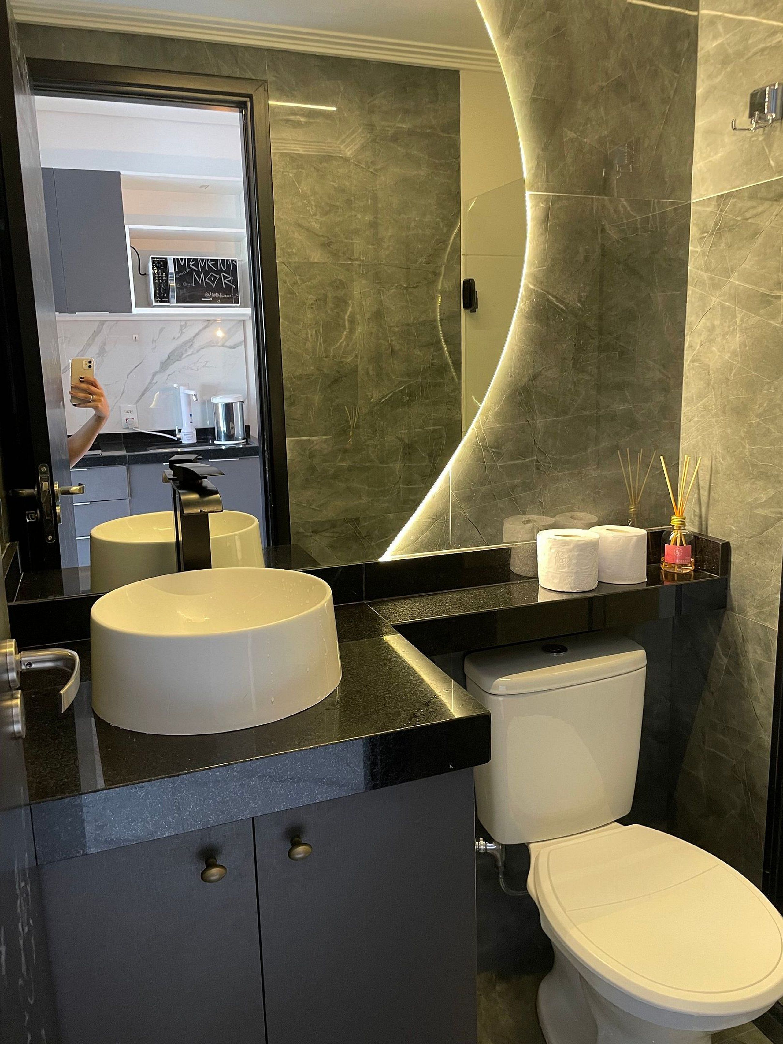 Un baño moderno con lavamanos redondo, inodoro y espejo curvo.