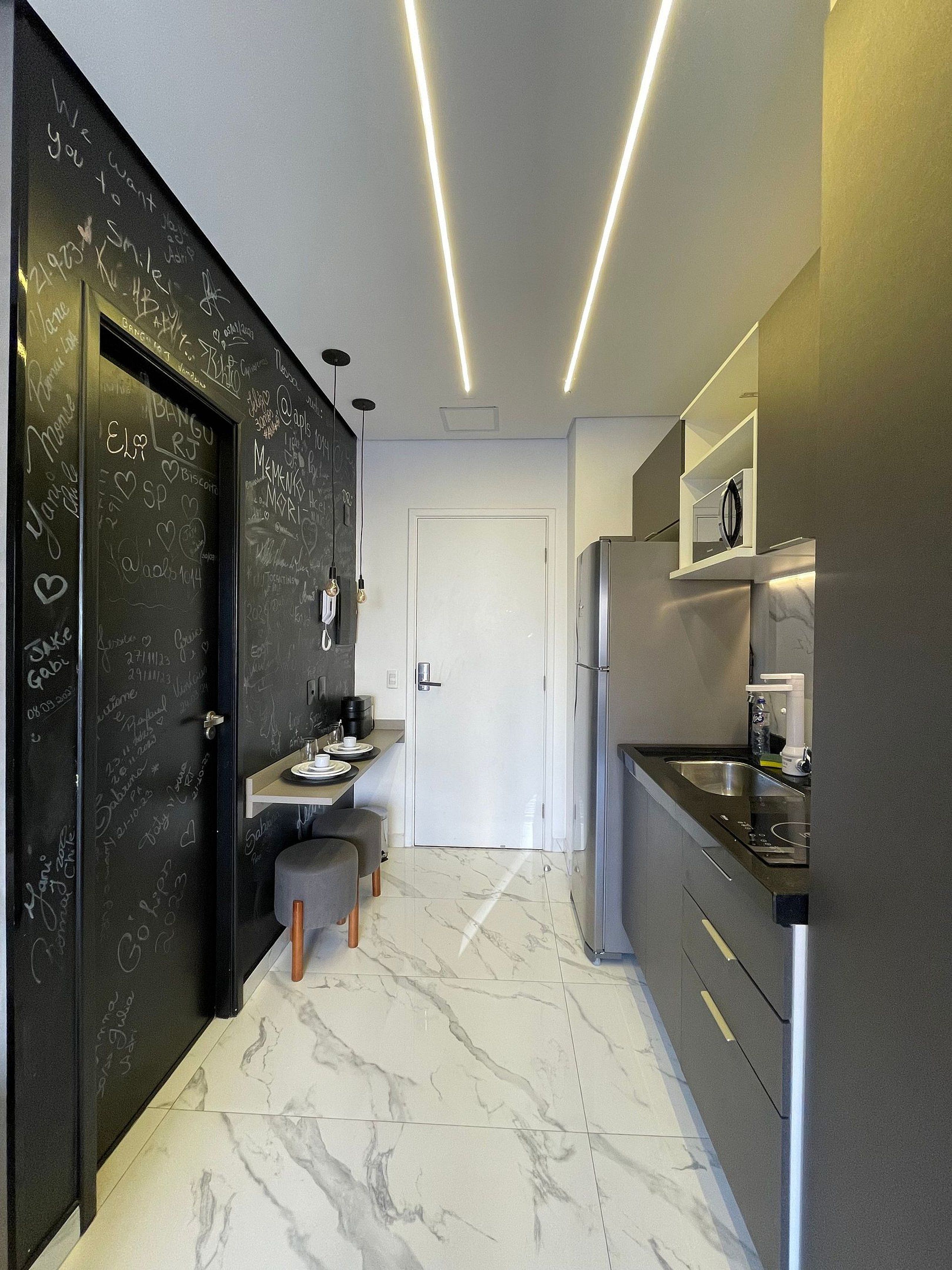 Una cocina moderna con piso de mármol, una pizarra con anotaciones y un refrigerador de acero inoxidable.