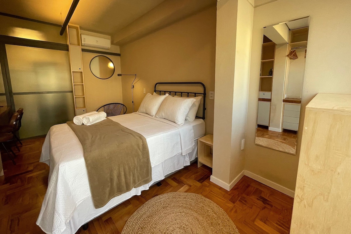 Een slaapkamer met een bed, een stoel, een nachtkastje, een lamp, een spiegel en een kledingkast.