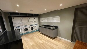 Een wasserette met vijf wasmachines, een wasbak en informatieposters aan de muur.