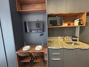 Une cuisine compacte équipée d’un four à micro-ondes, d’un évier et d’une étagère en bois au-dessus du plan de travail.