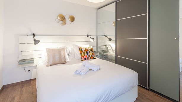 Un dormitorio moderno con una cama grande, lámparas de noche, un espejo y un armario.
