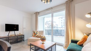 Un salón moderno con televisor, una mesa de centro, un sofá y un balcón con vistas a edificios.