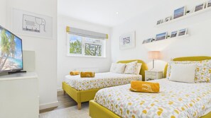 Habitación de hotel con dos camas, una televisión, una ventana con persianas y una pared con cuadros enmarcados.