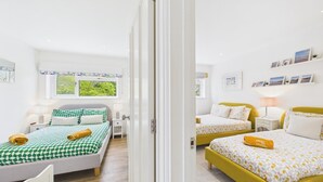 Habitación de hotel con dos camas, una ventana con vistas, una mesita de noche con lámpara y una pared con cuadros enmarcados.