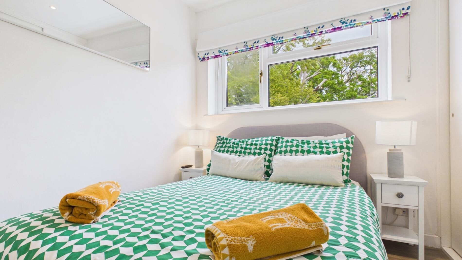 Ein Schlafzimmer mit einem Bett, zwei Nachttischen, einem Fenster mit Blick und einem Spiegel an der Wand.