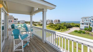 A wooden deck with outdoor furniture, a white railing, and a view of a residential area with houses and a body of water. - Calypso: Semi-Soundfront w/ Pool | Wind Over Waves (Salvo)