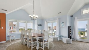 A dining area with a round table and chairs, large windows with a view, and a chandelier. - Calypso: Semi-Soundfront w/ Pool | Wind Over Waves (Salvo)