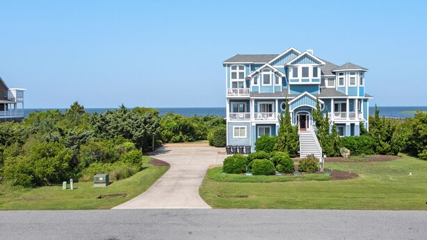 A large, two-story house with a front porch and a driveway leading to the entrance. - Calypso: Semi-Soundfront w/ Pool | Wind Over Waves (Salvo)