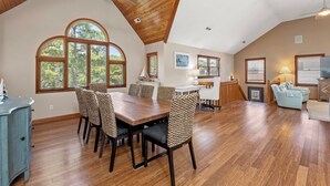 Amplia sala de estar con techo de madera, ventanas grandes, mesa de comedor y un sofá.