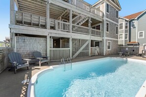 A pool area with a wooden deck, Adirondack chairs, and a staircase leading to a balcony. - Semper Surf: Private Pool, Hot Tub, Rec Room (Nags Head)