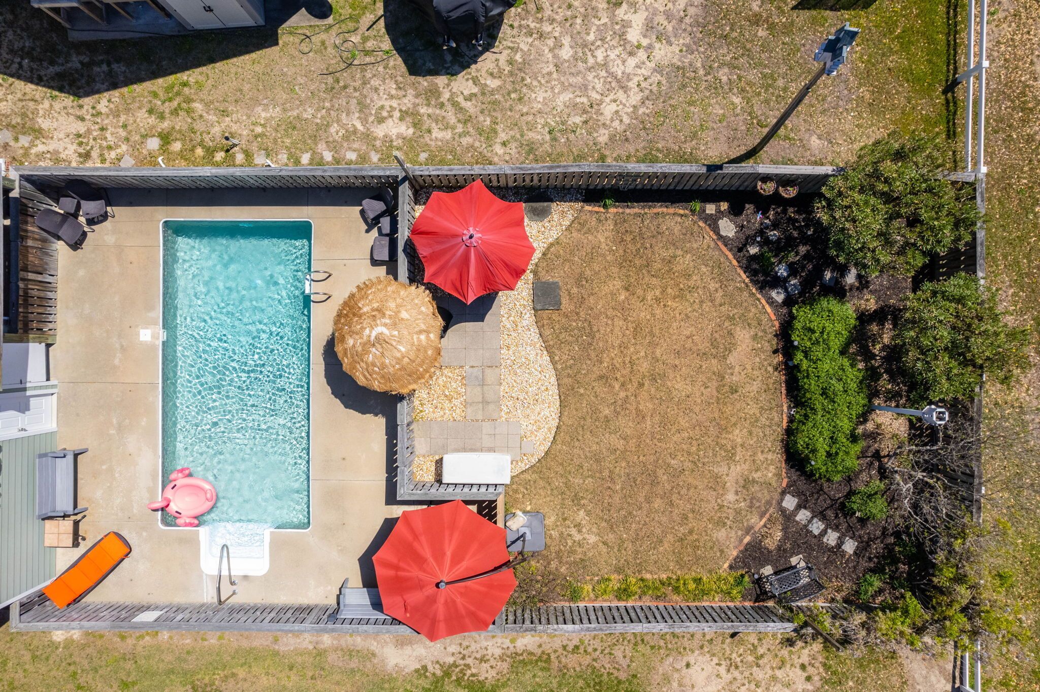 Vista aérea de un patio trasero con piscina, dos sombrillas rojas, un jacuzzi y una fogata.