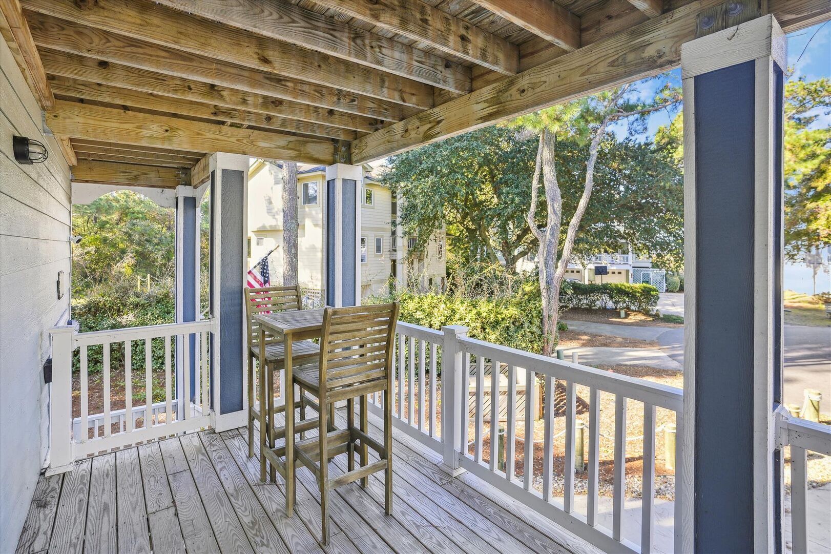 Une terrasse en bois avec une table et des chaises, une rambarde et une vue sur un quartier résidentiel, avec des arbres et des maisons.