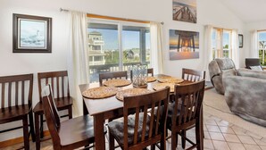 A dining area with a table set for four, surrounded by wooden chairs, with a view of a house through large windows.